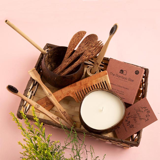 Eco-friendly gift hamper with neem toothbrush, bamboo tongue cleaner, comb, coconut bowl & cutlery, bamboo earbuds, and soy wax candle.