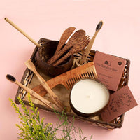 Eco-friendly gift hamper with neem toothbrush, bamboo tongue cleaner, comb, coconut bowl & cutlery, bamboo earbuds, and soy wax candle.